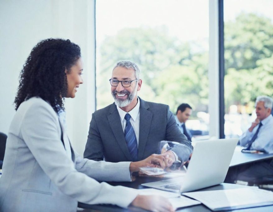 Two professionals discussing over a laptop in a bright office setting.