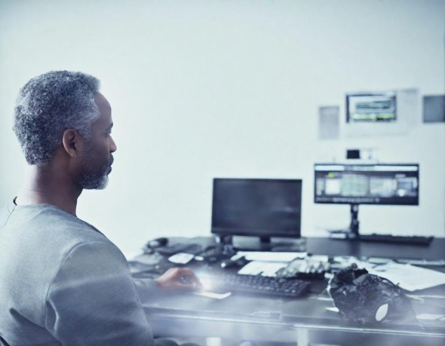 A man sits at a desk, focused on a computer screen with cameras nearby.